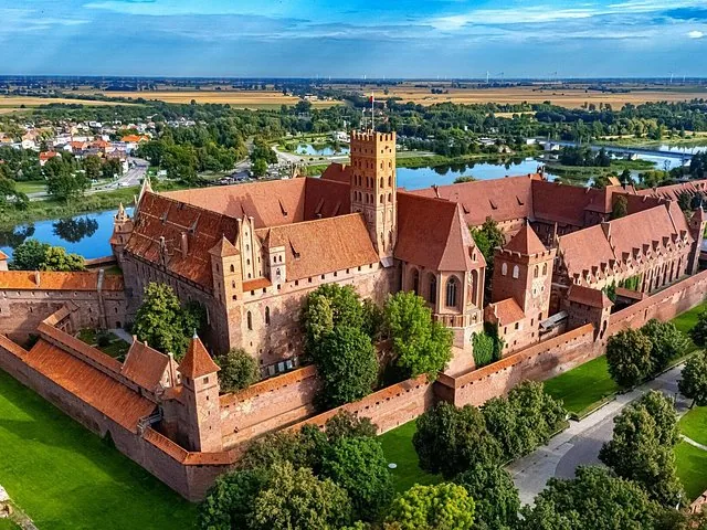 Aerial view of Malbork Castle complex with river and fields.