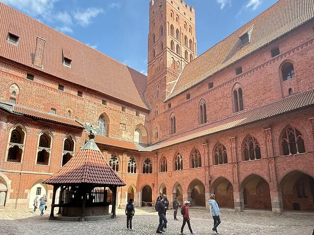 Tourists walking in the sunny courtyard of Malbork Castle.