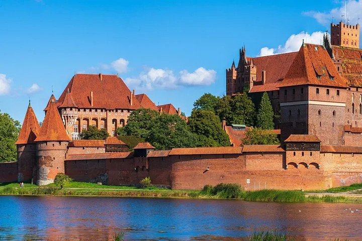 Exterior view of Malbork Castle's red brick walls beside a river.