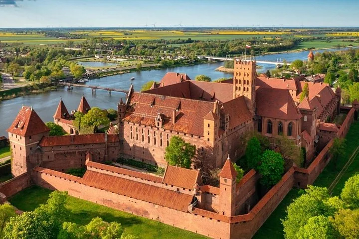 High aerial view of Malbork Castle, river, and surrounding green landscape.